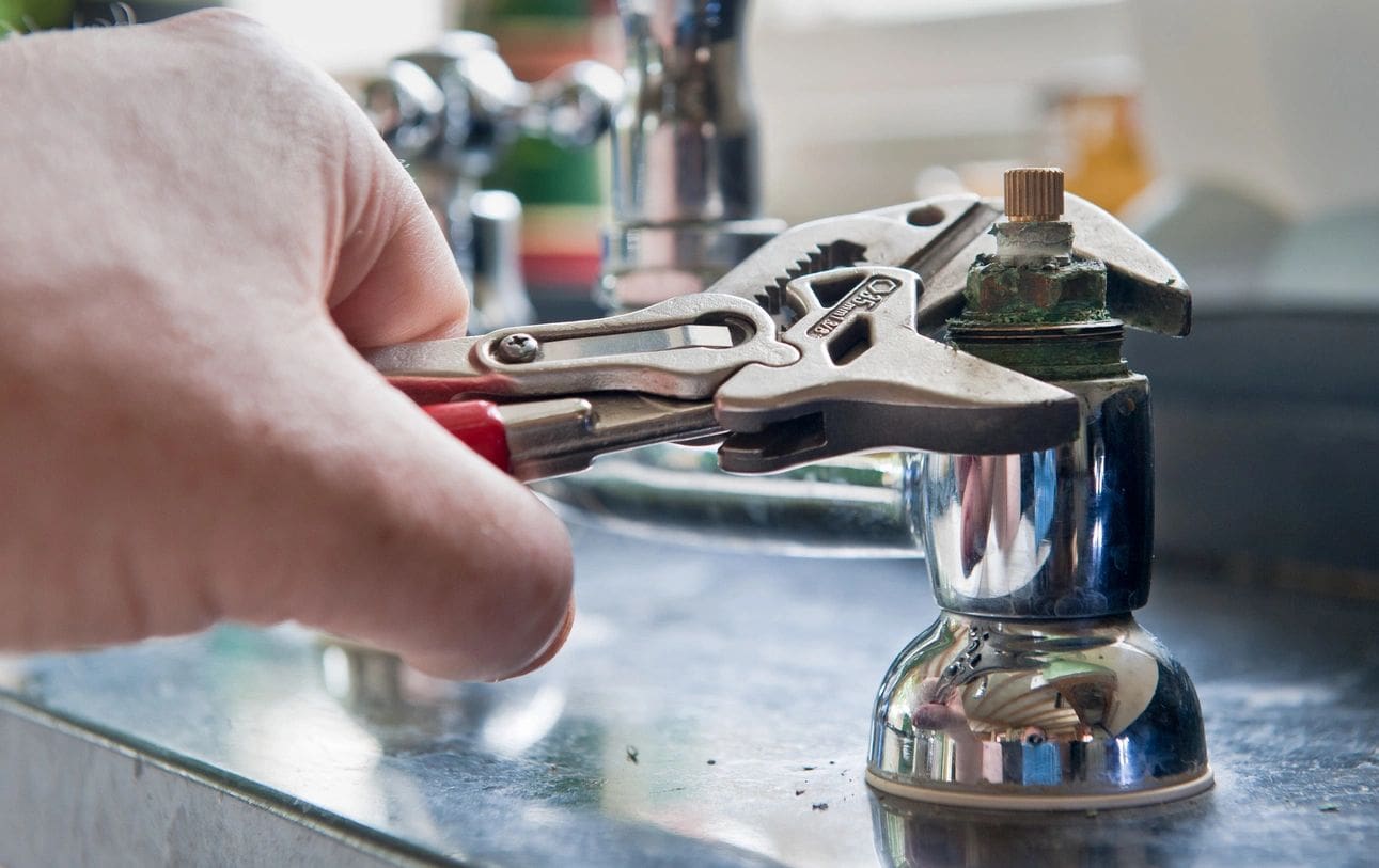 A person holding a pair of pliers over the top of a faucet.